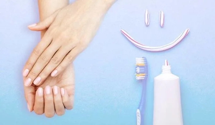 Scrubbing stained fingernails with a toothbrush and whitening toothpaste to remove yellow polish marks.