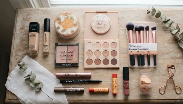 Flat lay of affordable beginner makeup products including foundation, brushes, eyeshadow palette, and mascara. Flat lay of affordable beginner makeup products including foundation, brushes, eyeshadow palette, and mascara.