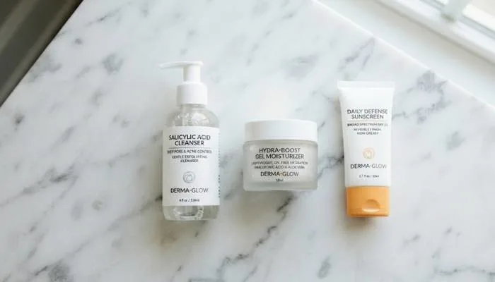 Flat lay of a salicylic acid cleanser, lightweight gel moisturizer, and sunscreen on a clean marble surface. Flat lay of a salicylic acid cleanser, lightweight gel moisturizer, and sunscreen on a clean marble surface.