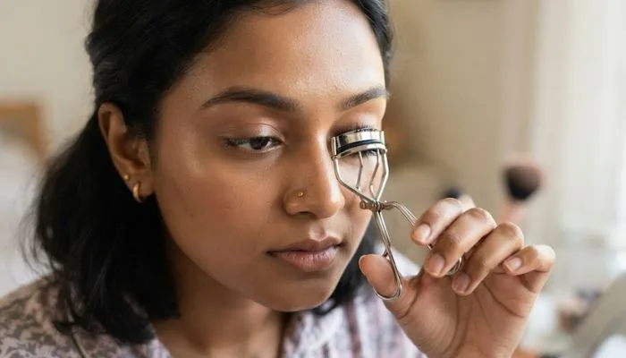 Close-up shot of a person correctly positioning an eyelash curler at the base of their eyelashes before curling.