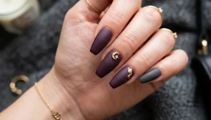 A close-up shot of almond or coffin-shaped acrylic nails in dark plum and charcoal grey with minimal gold foil or a single charm.