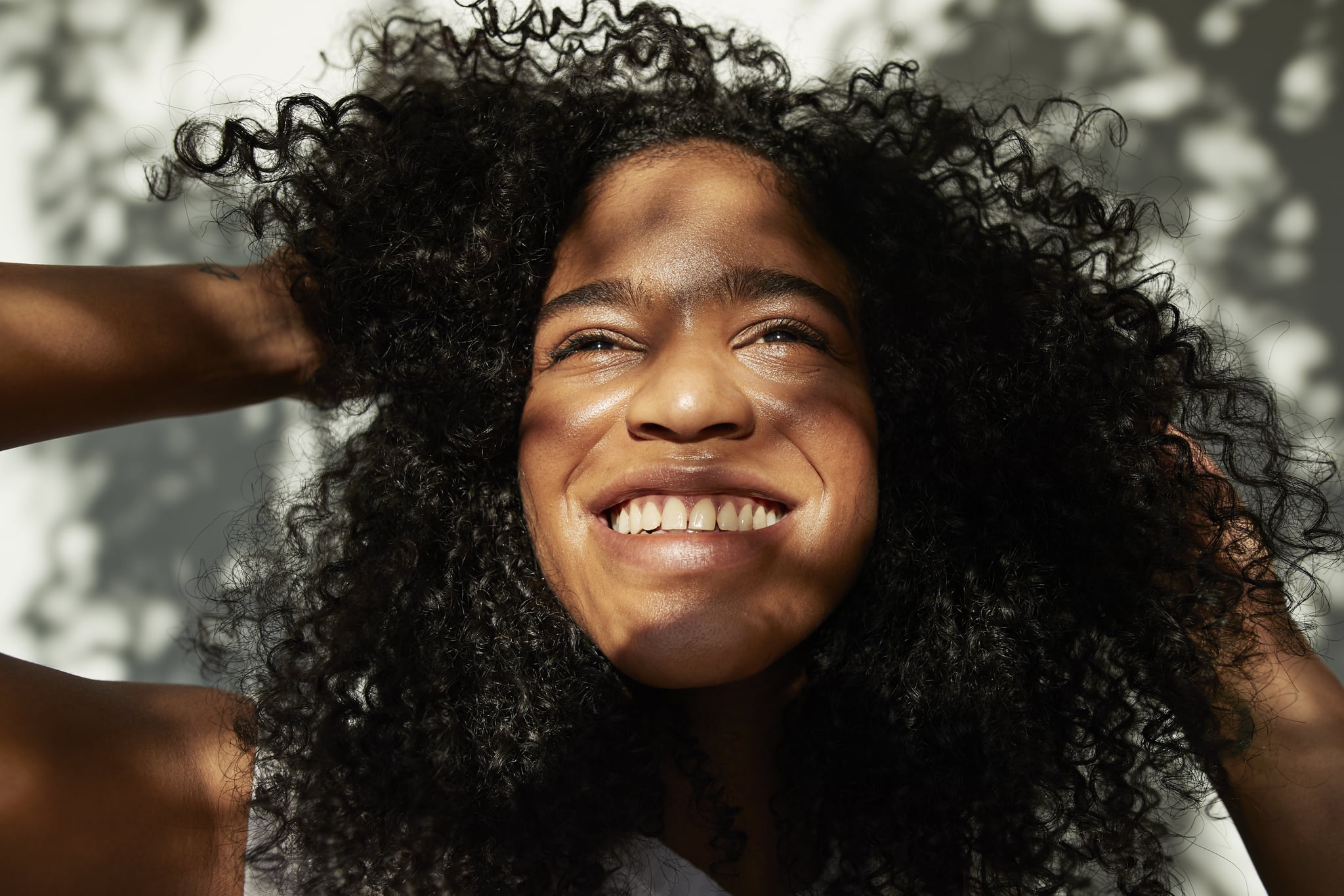 Smiling young woman looking up while standing against white wall